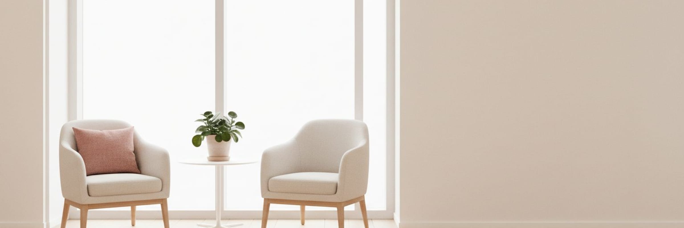 A quiet meeting nook with two pale chairs, a small round table and a green plant beside a bright window.